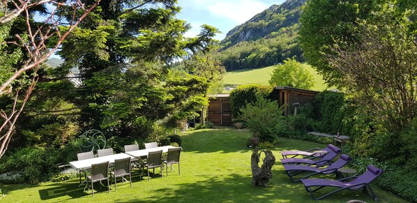 Un jardin avec une table et des chaises, une structure en bois et une vue sur une montagne.