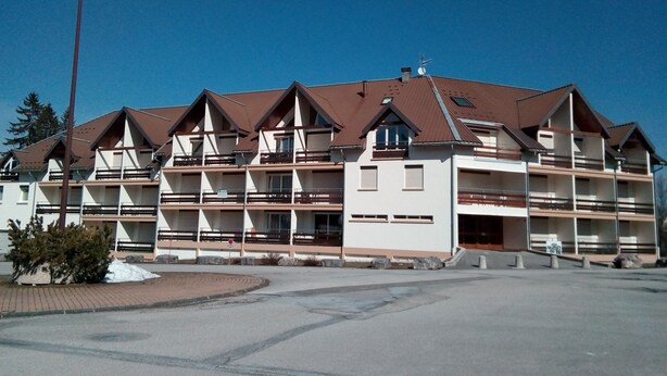 Ein mehrstöckiges Hotel mit einer symmetrischen Fassade, Balkonen und einem Parkplatz davor.