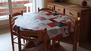 Ein Essbereich mit einem Tisch für vier Personen, einem Fernseher auf einer Holzkommode und Blick auf einen Garten durch ein großes Fenster.