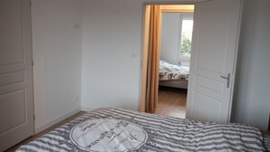 Een slaapkamer met een bed, een deur die naar een andere kamer leidt en een raam met gordijnen.