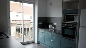 Een moderne keuken met een schuifdeur van glas naar een balkon, een ingebouwde magnetron, oven en koffieapparaat.
