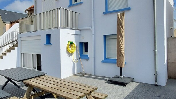 Een gebouw met twee verdiepingen en een overdekt terras, een houten bankje en een waterslang.
