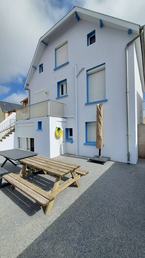 Een gebouw met twee verdiepingen en een overdekt terras, een houten bankje en een waterslang.