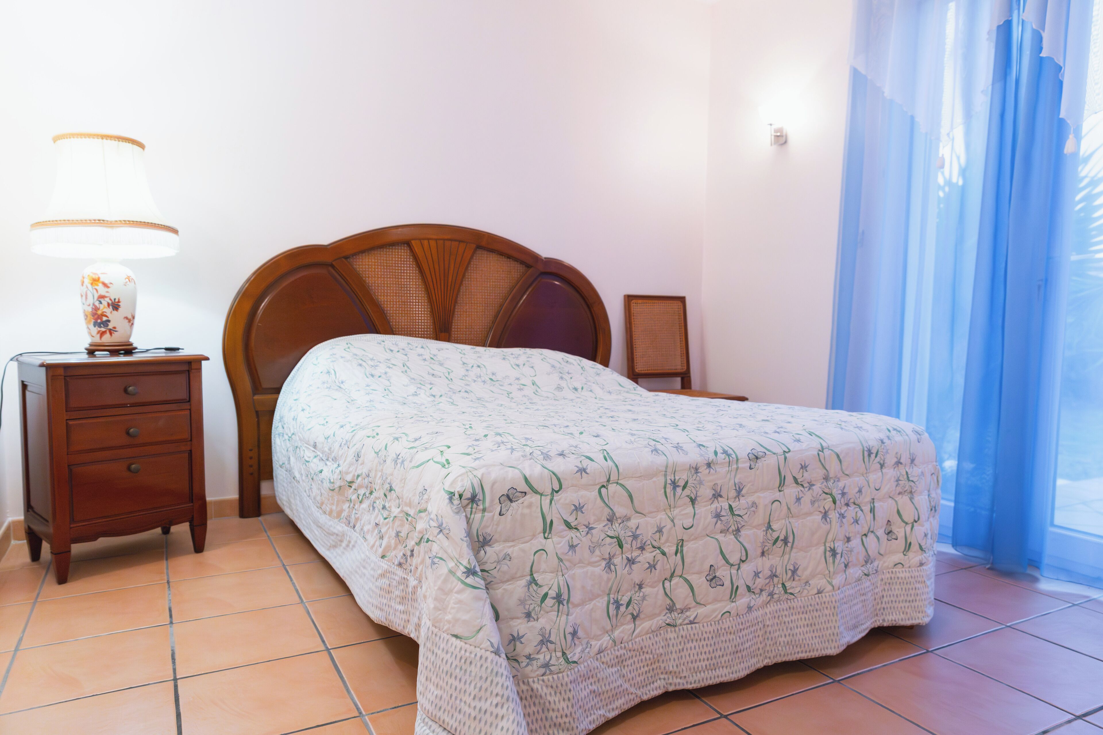 Une chambre à coucher avec une tête de lit en bois, une table de chevet avec une lampe et une fenêtre ornée de rideaux bleus.