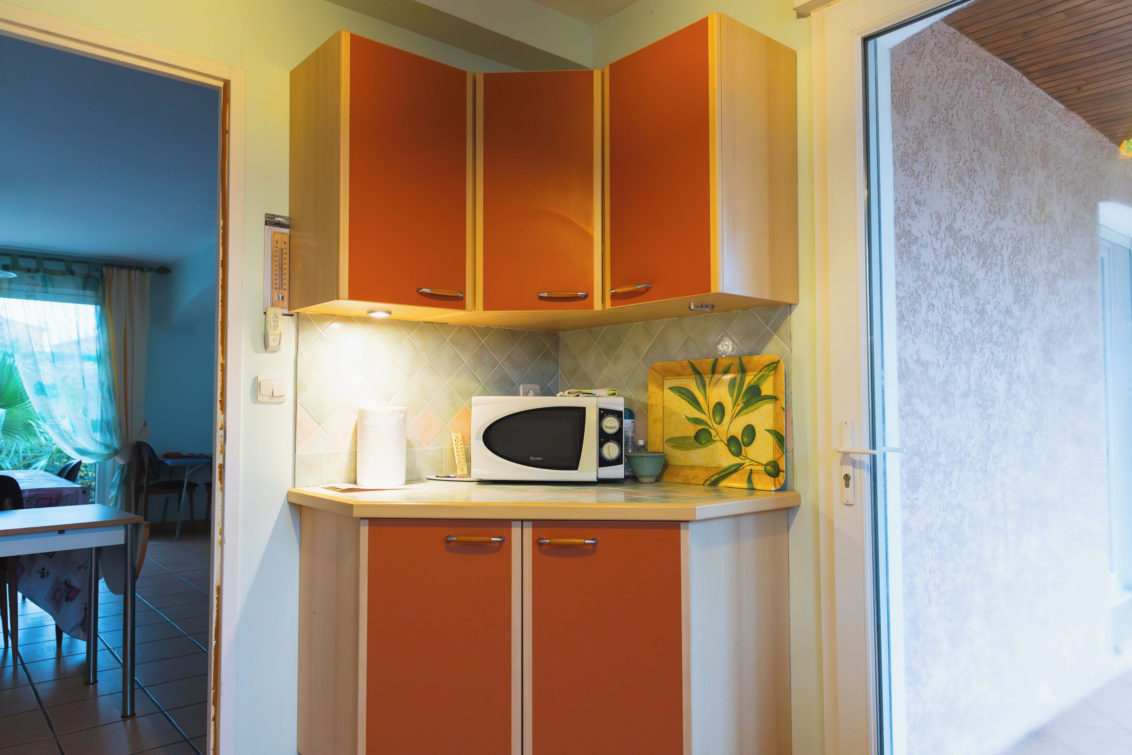 A compact kitchen with orange cabinets, a microwave, and a small countertop.