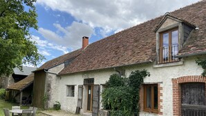 A rustic house with a tiled roof, a wooden door, and a small garden area with a table and chairs. - Le Colombier Guesthouse (Concriers)