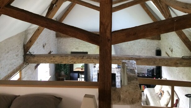 A room with a high ceiling supported by wooden beams, a bed with a pillow, a lamp on a bedside table, and a window. - Le Colombier Guesthouse (Concriers)
