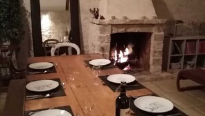 A wooden dining table set for six with plates, cutlery, and wine glasses. A fireplace is visible in the background. - Le Colombier Guesthouse (Concriers)