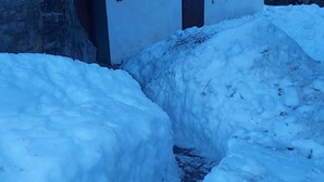 Un espace extérieur enneigé avec un petit ruisseau, un bâtiment blanc aux volets rouges et une clôture en bois.