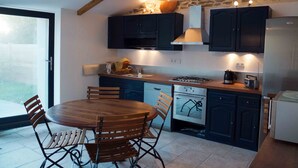 A modern kitchen with dark cabinets, a wooden dining table, and a stone wall. - Fisherman's house Gulf of Morbihan (Sarzeau)