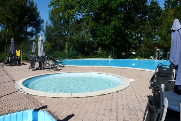 A circular pool with a surrounding paved area, equipped with lounge chairs and umbrellas. - House with swimming pool in condominium (Saint-Julien-En-Born)