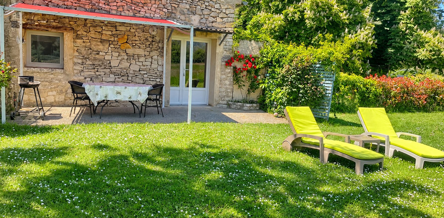 Une maison en pierre avec un patio couvert, une table et des chaises, ainsi que deux fauteuils de jardin jaunes.