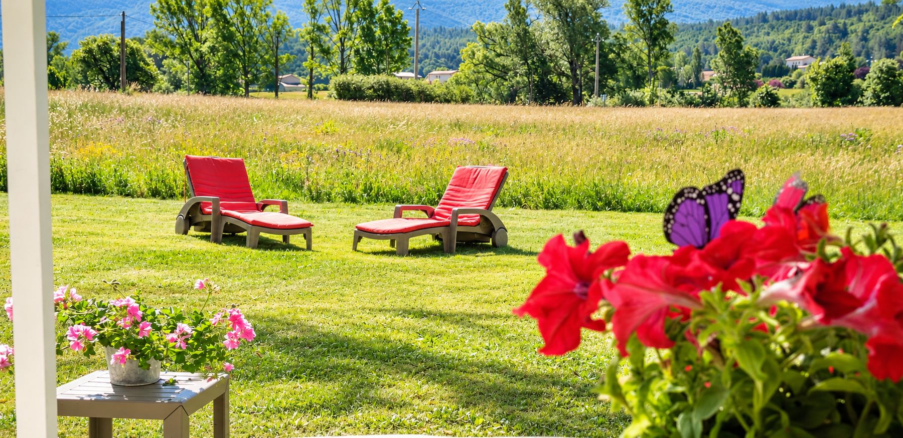 A grassy outdoor area with two red lounge chairs and a table with pink flowers.