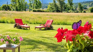 A grassy outdoor area with two red lounge chairs and a table with pink flowers.