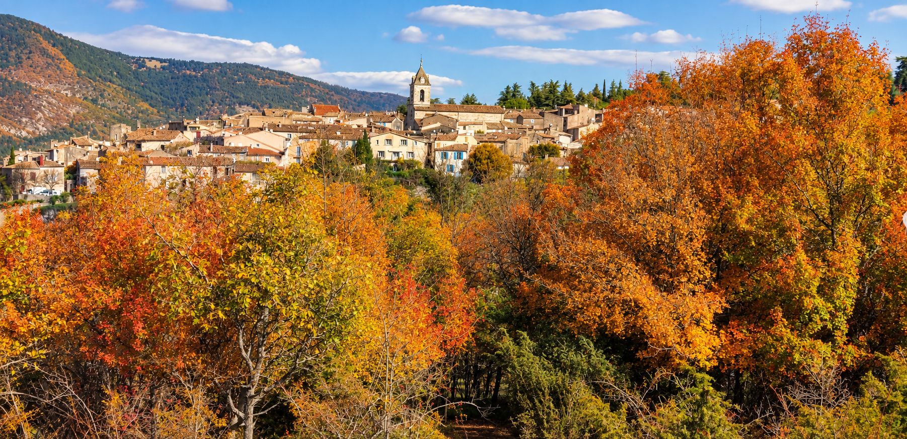 Ein Dorf mit Gebäuden und einer Kirche auf einem Hügel, umgeben von Herbstlaub.