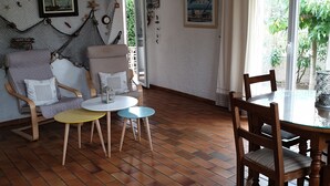 A living room with a wooden floor, a ceiling fan, a dining table with chairs, and a large window with curtains.