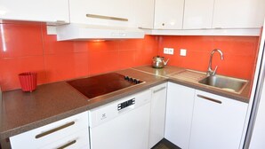 A compact kitchen with white cabinets, a red backsplash, a built-in oven, a sink, and a dishwasher. - Risoul 4 bedroom duplex sleeps 11, at the foot of the slopes, summer winter (Risoul)
