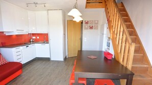 A compact kitchen with white cabinets, a wooden dining table, and a red sofa. - Risoul 4 bedroom duplex sleeps 11, at the foot of the slopes, summer winter (Risoul)