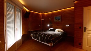A bedroom with a wooden floor, a bed with a polka dot bedspread, a nightstand, a lamp, and a painting on the wall. - 4 stars - High standing air conditionned apartment, heated swimming pool, Geneva (Collonges sous Salève)