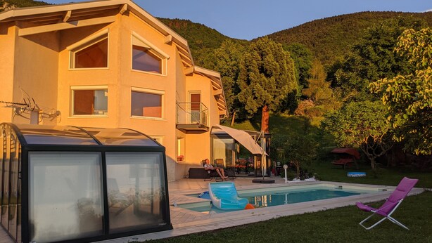 A two-story house with a swimming pool, a covered patio, and a view of a forested hill. - 4 stars - High standing air conditionned apartment, heated swimming pool, Geneva (Collonges sous Salève)