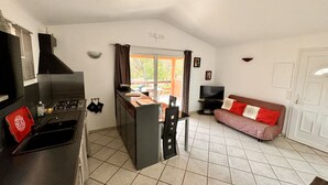 Un espacio habitable compacto con kitchenette, comedor y zona de estar con sofá.