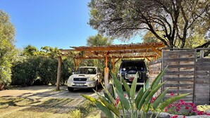 Un vehículo estacionado bajo una pérgola de madera en un jardín con diversas plantas y flores.