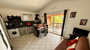Un espacio habitable compacto con kitchenette, zona de comedor y sofá con cojines rojos.