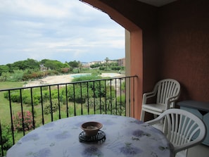 Un balcon avec une table et des chaises, donnant sur une piscine et un espace verdoyant.