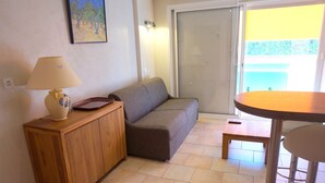 A room with a sofa, a wooden cabinet, a table, and a sliding glass door leading to an outdoor area.