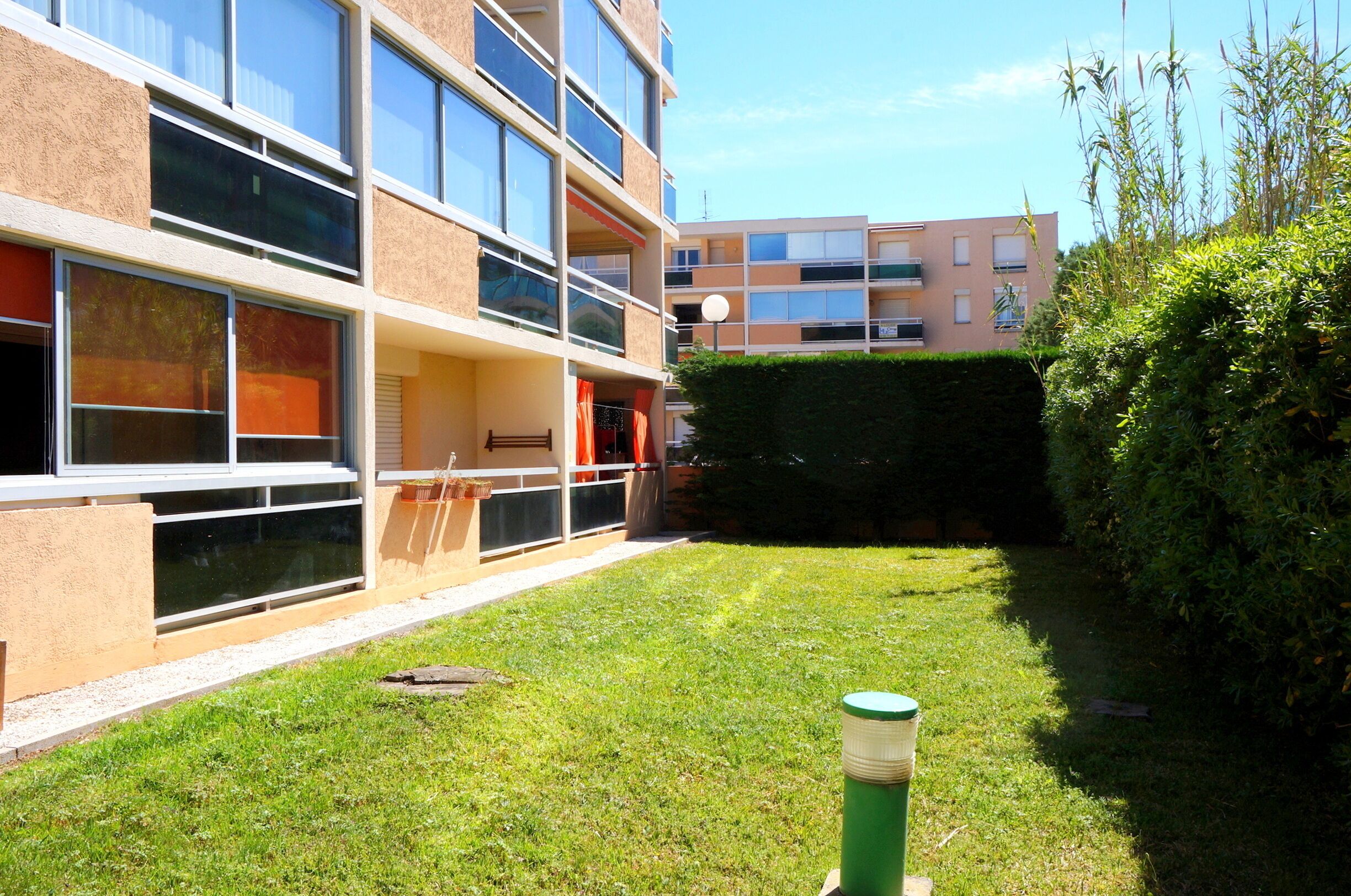 Un bâtiment moderne doté de nombreux balcons, d’une cour verdoyante et d’une haie.