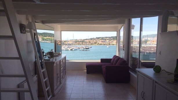 Een kamer met uitzicht op een haven, een paarse bank, een keukenhoek en een ladder.