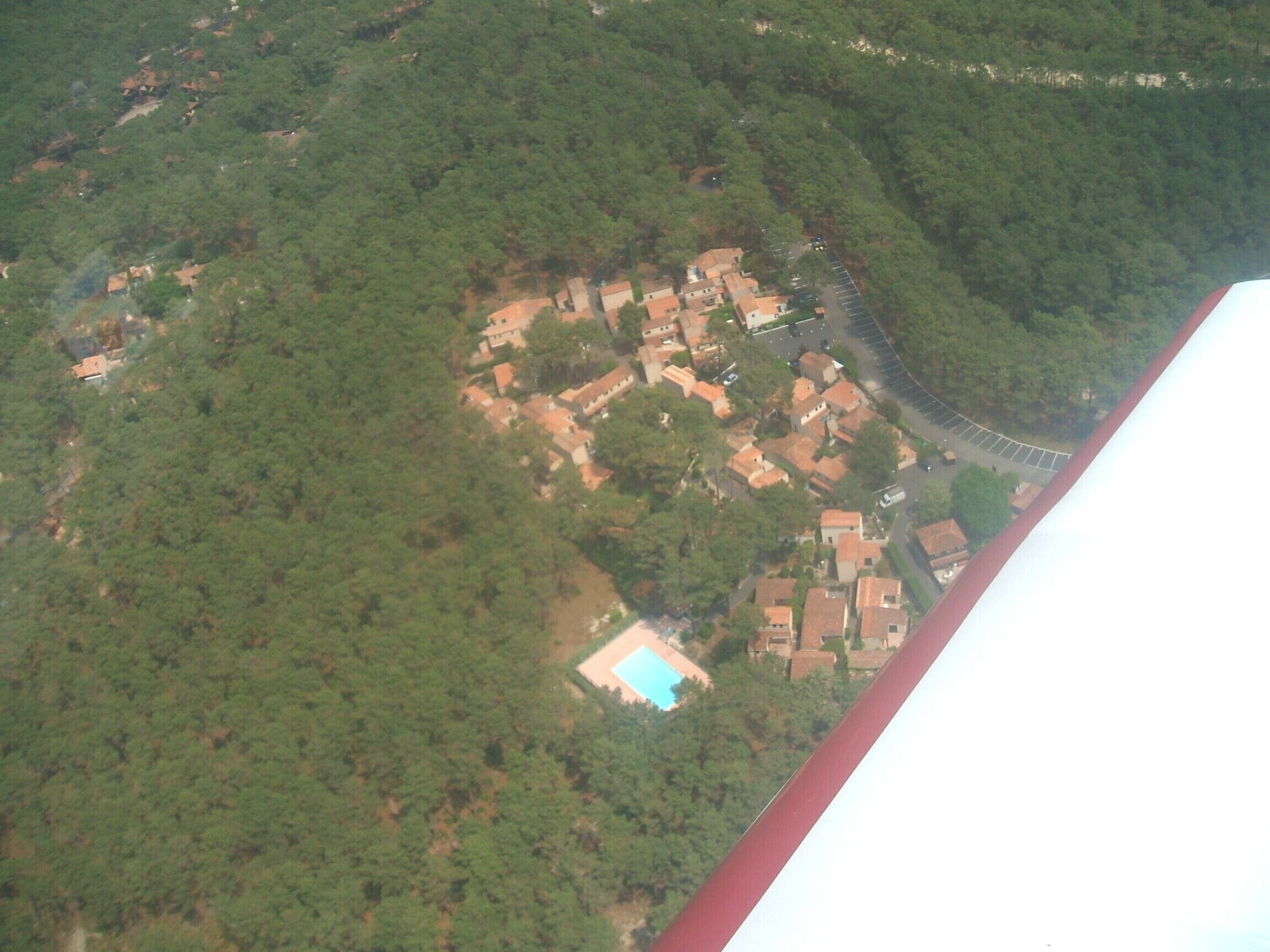 An aerial view of a residential area with houses, a swimming pool, and a curved road.