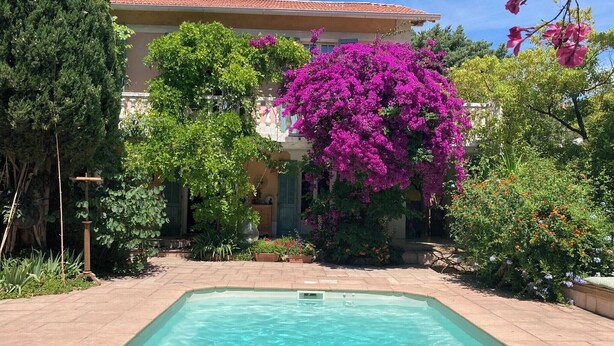 En swimmingpool med ett klart, blått vatten, omgiven av frodig grönska och vackra, lila bougainvilleablommor.