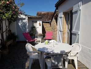 Une terrasse avec une table ronde et quatre chaises, un mur en pierre et un bâtiment blanc avec une porte.