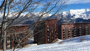 Un paisaje nevado con una cadena montañosa al fondo y un edificio con múltiples balcones y ventanas.