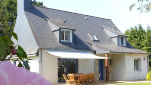 Ein Haus mit geneigtem Dach, einer Terrasse mit Tisch und Stühlen sowie einer großen Blume im Vordergrund.