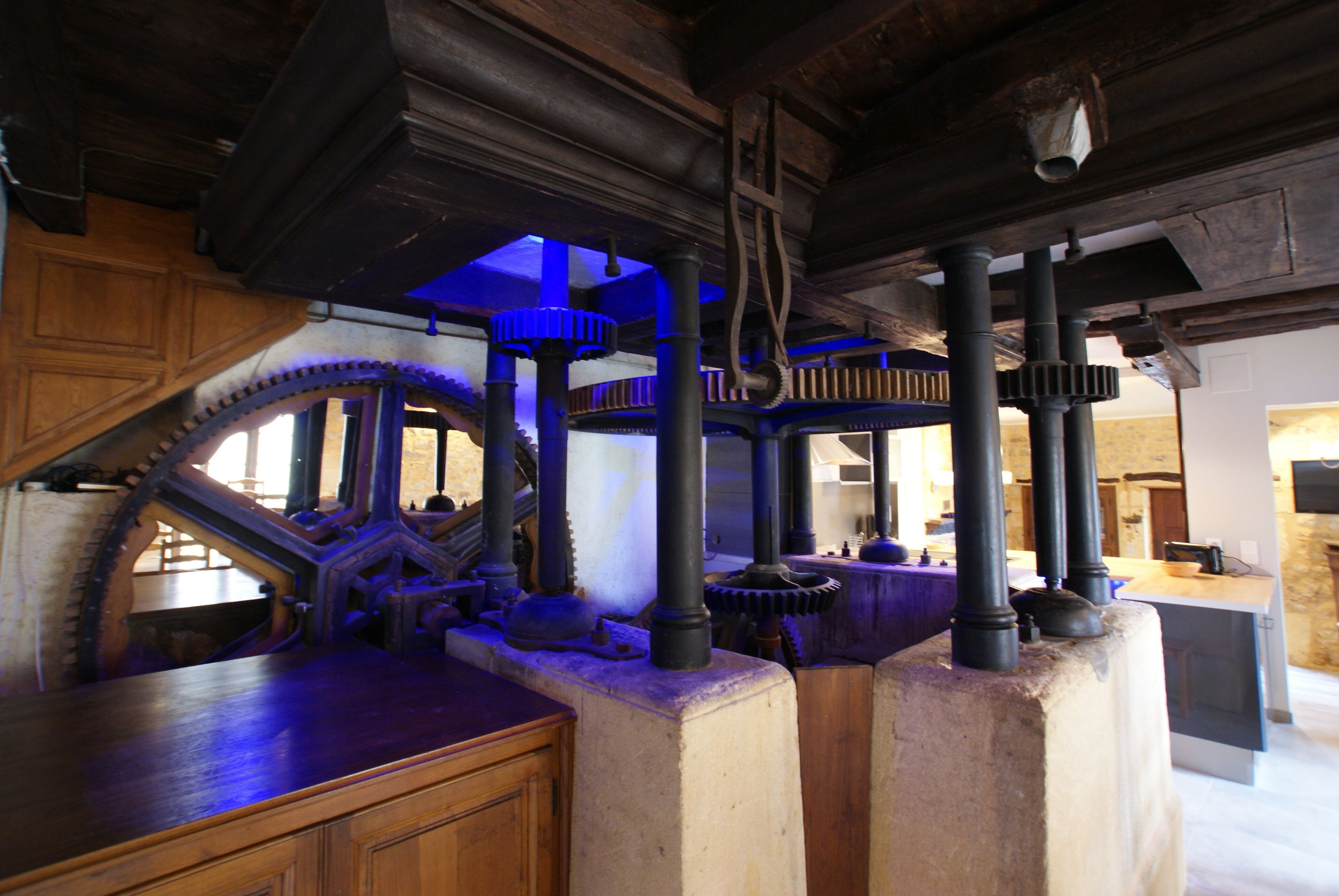 A room with exposed wooden beams, a large mechanical gear, and a stone pillar.