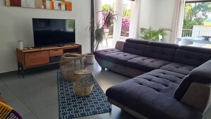 A modern living room with a large flat-screen TV, a dark-colored sofa, and a coffee table with a woven base. - Family villa with swimming pool, between sea and mountains. (Prunelli-di-Fiumorbo)