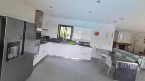 A modern kitchen with white cabinetry, a stainless steel refrigerator, and a large window. - Family villa with swimming pool, between sea and mountains. (Prunelli-di-Fiumorbo)