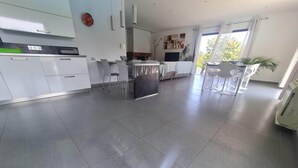 A modern kitchen with white cabinets, a central island, and a dining area with chairs. - Family villa with swimming pool, between sea and mountains. (Prunelli-di-Fiumorbo)