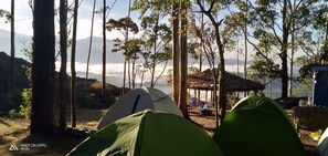 Un camping con tiendas de campaña, una estructura de techo de paja y vistas a un paisaje montañoso.