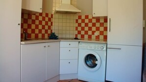 A compact kitchen with a washing machine, white cabinets, and a red and white checkered backsplash. - Apartment in the heart of Vaucluse close to the tourist attractions of Vaucluse (Loriol du Comtat)