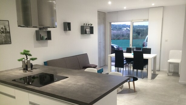 A modern kitchen with a central island, dining area with chairs, and a view of the outdoors.