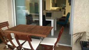 A dining area with a wooden table and chairs, a sliding glass door leading to a kitchen, and a small potted plant.