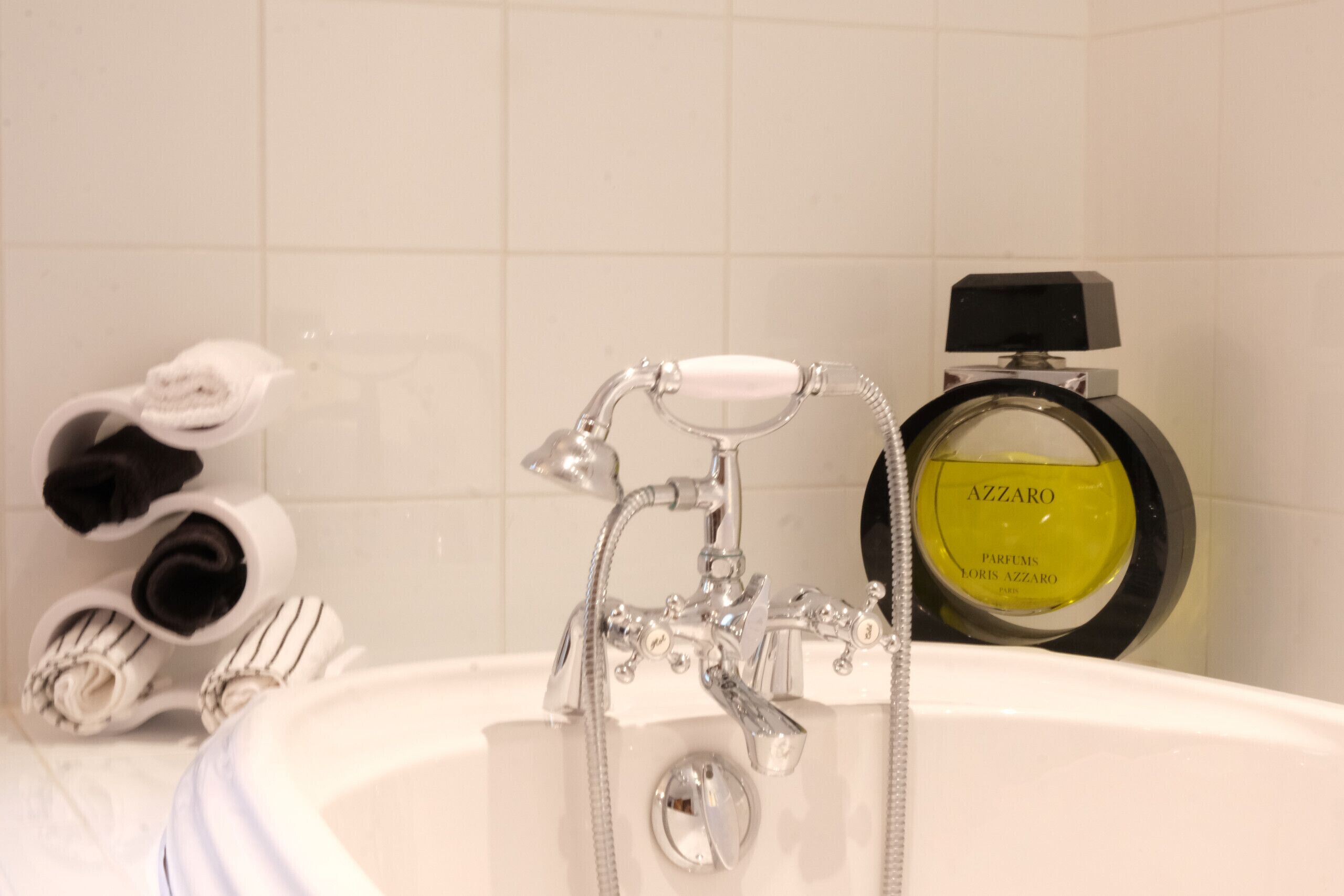 Un bagno con una vasca, un lavandino e una bottiglia di profumo Azzaro.