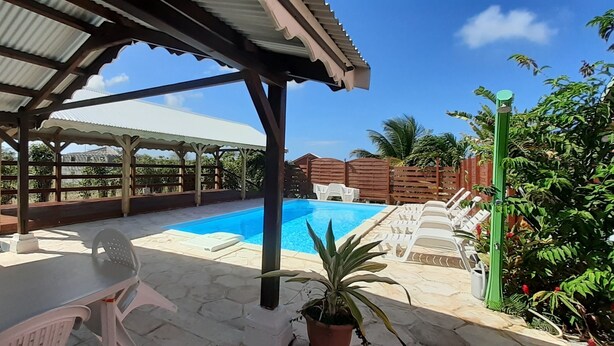 A covered outdoor area with a pool, lounge chairs, and a table.