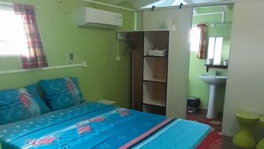 A bedroom with a bed, a wardrobe, a small bathroom, and a window with curtains.