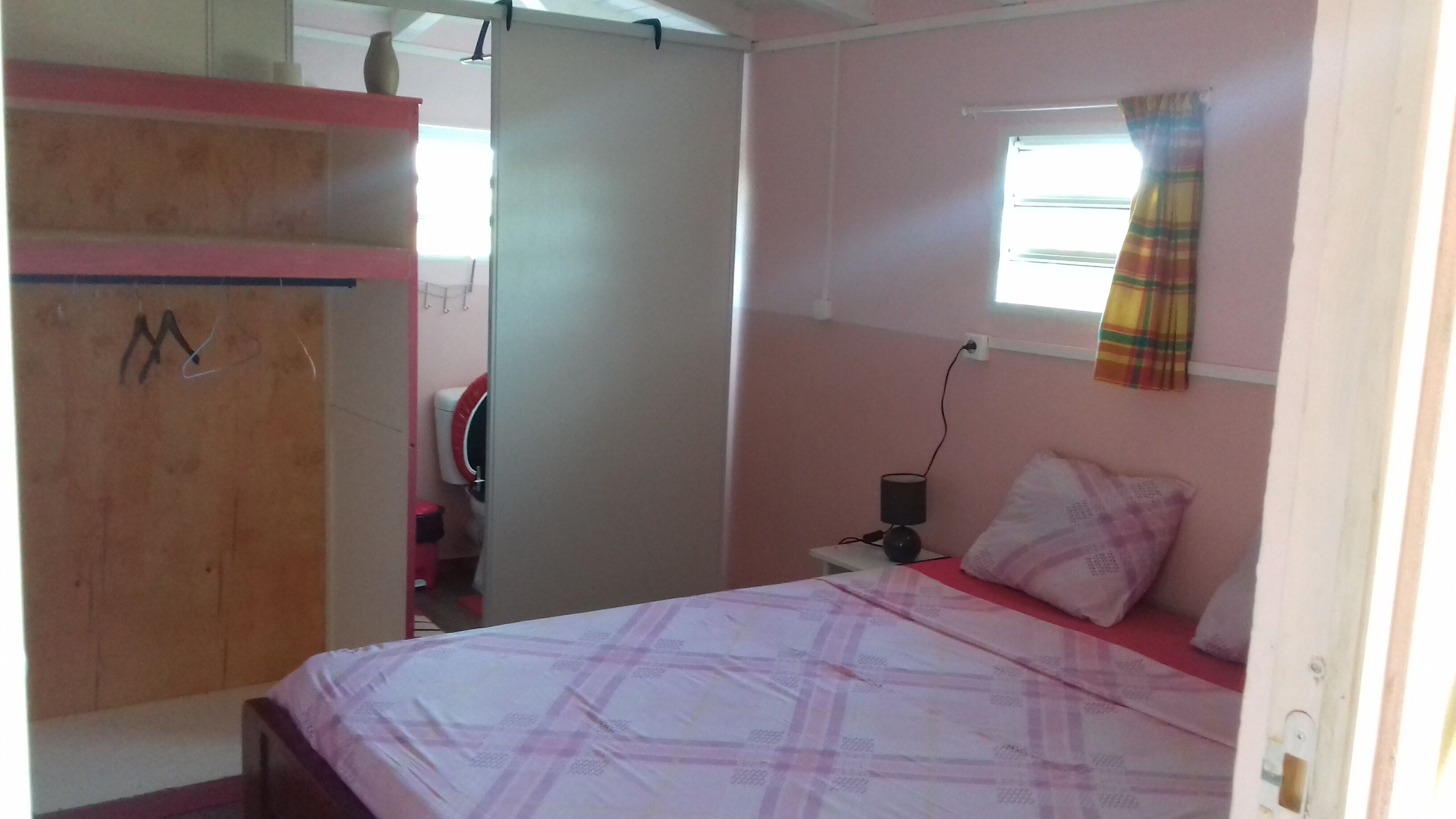 A bedroom with a bed, a wardrobe, a window with curtains, and a bedside table with a lamp.