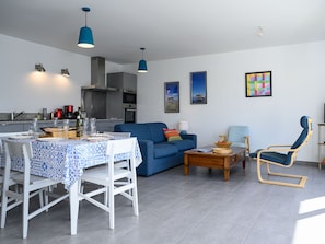 A modern living room with a blue sofa, a dining table with chairs, a wooden coffee table, and a blue rocking chair.