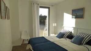 A bedroom with a bed, a chair, a nightstand, a lamp, and a window with curtains. - Kervegan magnifique villa vue mer à Pleumeur Bodou (PLEUMEUR BODOU)